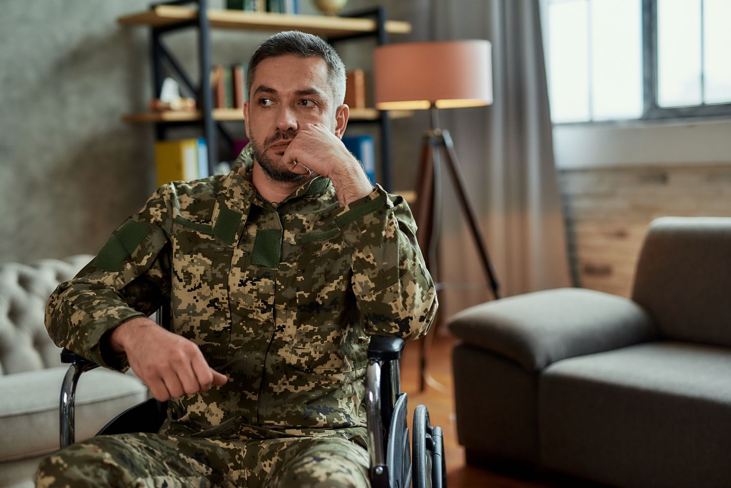 Middle aged thoughtful military man in a wheelchair looking away during therapy session. Disabled soldier suffering from depression, psychological trauma. PTSD concept. Horizontal shot